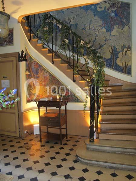 Escalier intérieur en bois avec rampe ornée de feuillage, décoré de fresques murales et éclairé par des lumières tamisées.