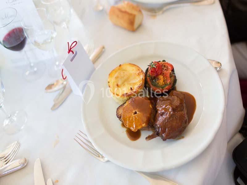 Assiette contenant une pièce de viande en sauce, un gratin de pommes de terre et des légumes grillés, sur une table dressée.