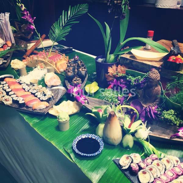 Buffet décoratif avec sushis, fleurs exotiques et statues sur une table recouverte de feuilles vertes.