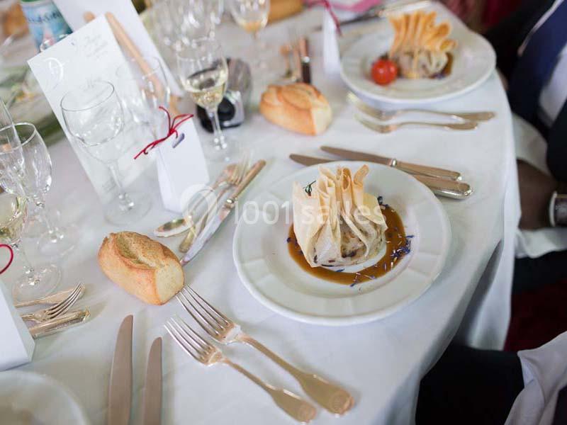 Assiette dressée avec une aumônière sur sauce, entourée de couverts, verres et pains sur une table élégante.
