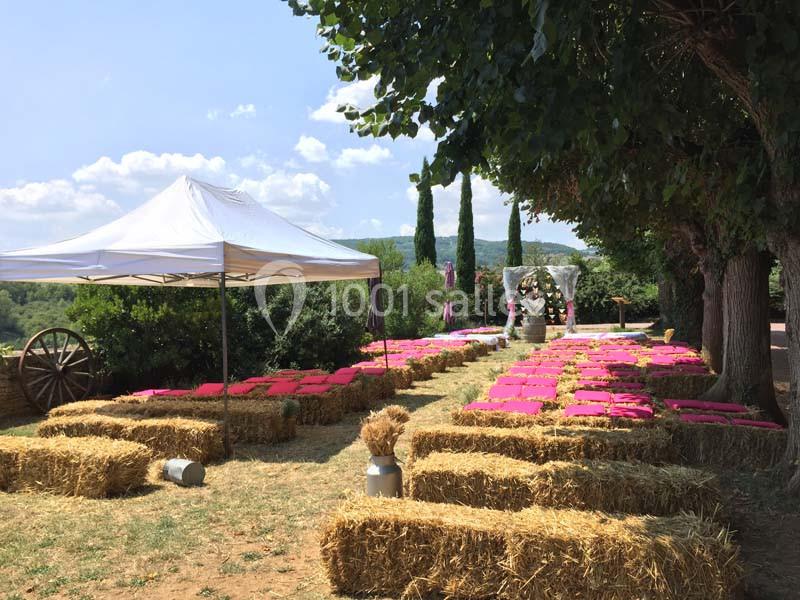 Chaises en bottes de paille avec coussins roses disposées en extérieur sous des arbres pour une cérémonie en plein air.
