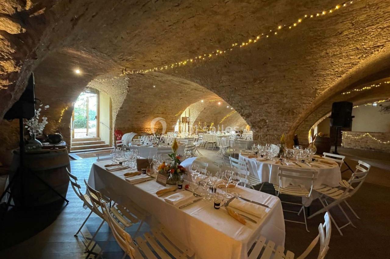 Salle voûtée en pierre décorée de guirlandes lumineuses, avec tables dressées pour un événement festif.