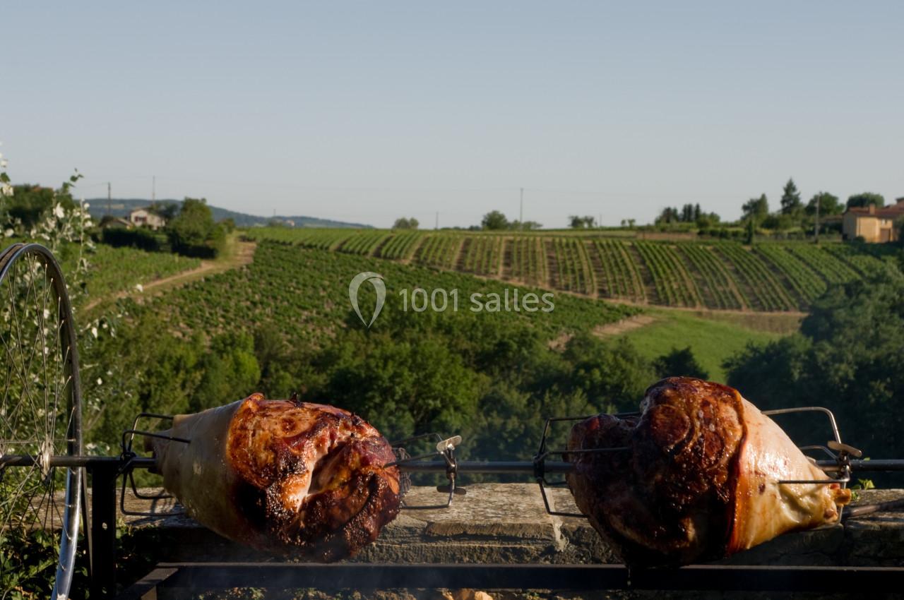 Deux morceaux de viande rôtissent sur une broche devant un paysage de vignobles sous un ciel dégagé.
