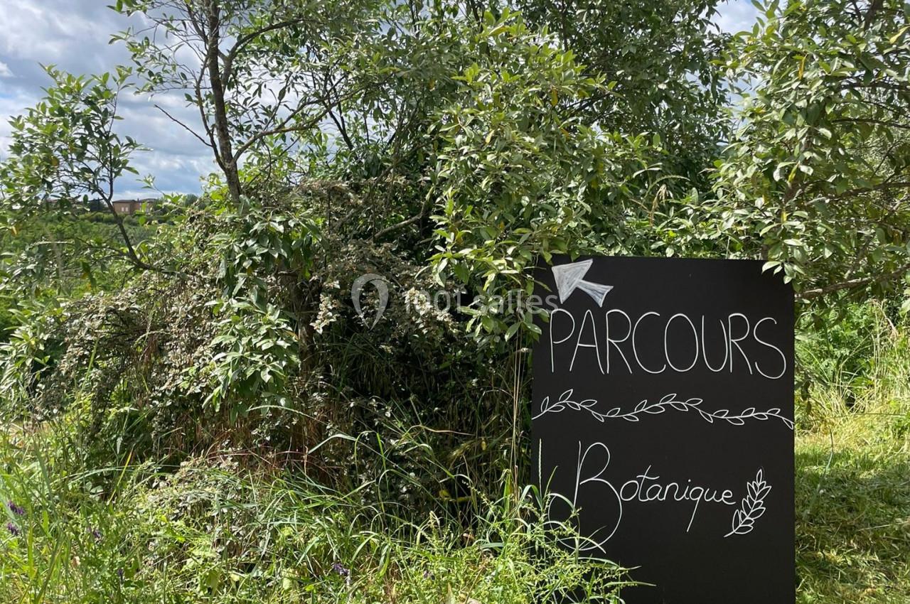 Panneau indiquant un parcours botanique, placé devant des arbustes dans un environnement naturel.