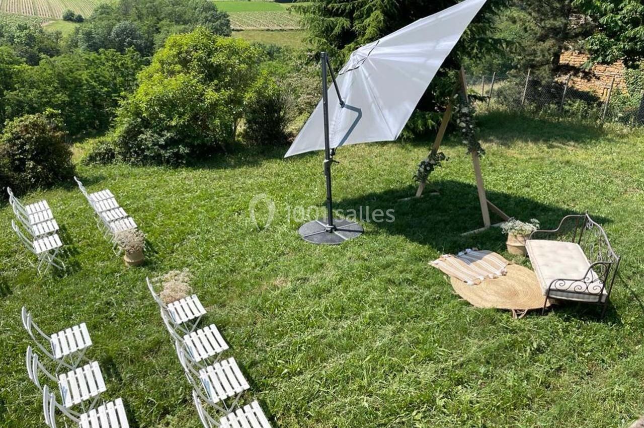 Chaises blanches alignées sur une pelouse, avec un parasol, un tapis et un banc décoratif en arrière-plan.