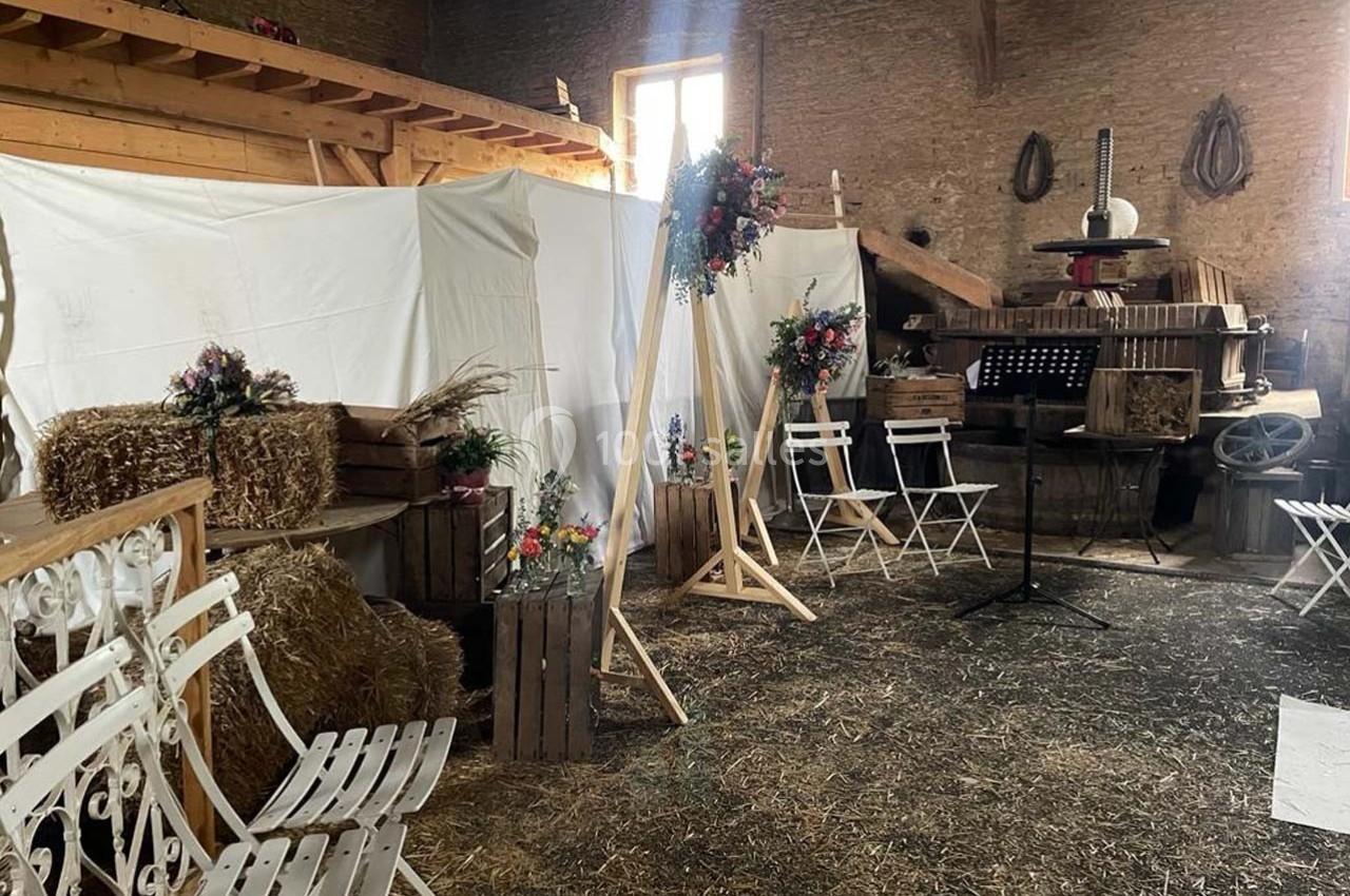 Intérieur d'une grange aménagée avec des bottes de foin, des chaises blanches et des décorations florales.
