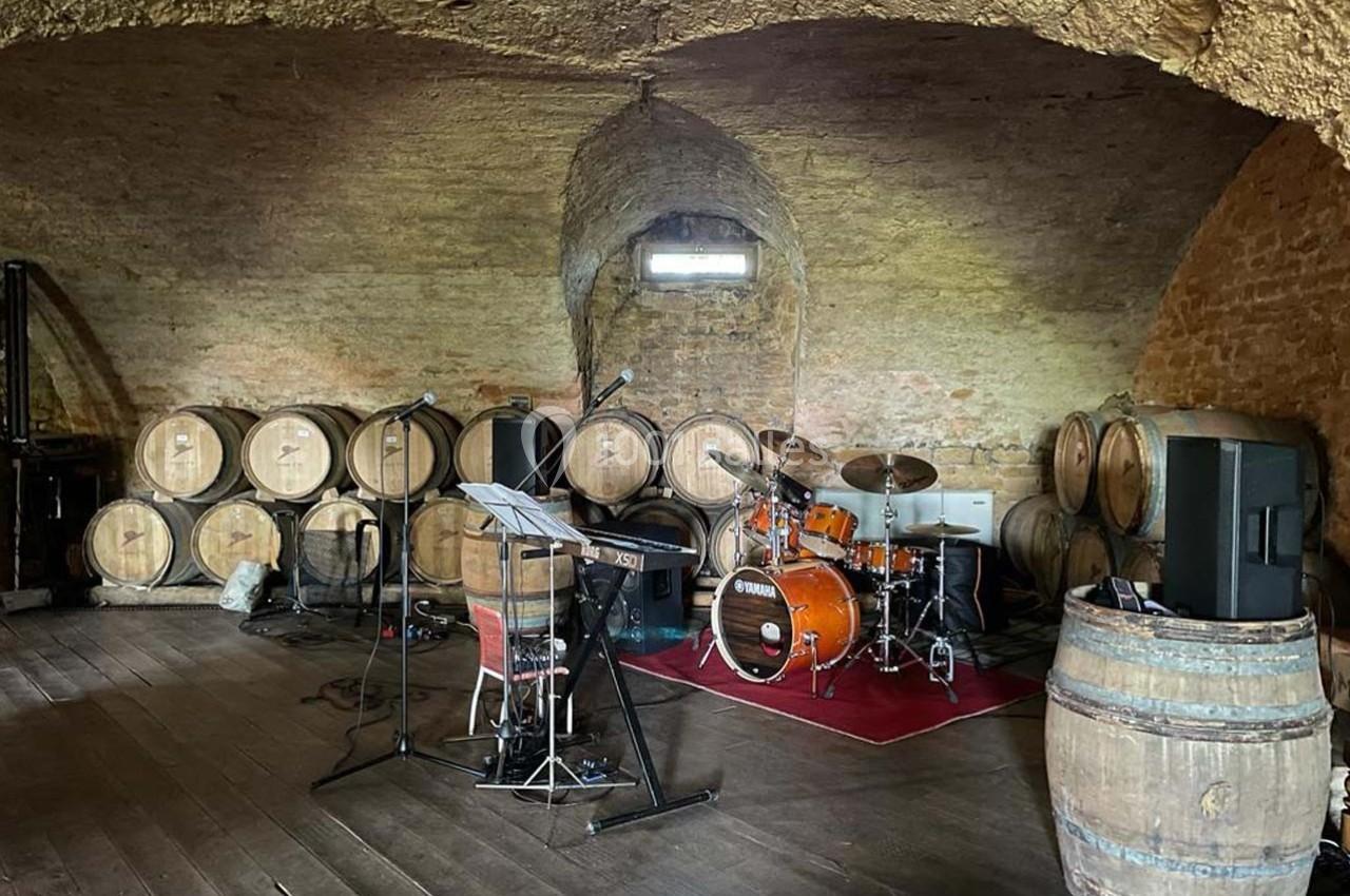 Salle voûtée avec barriques en bois, équipée d'instruments de musique dont une batterie et des micros.
