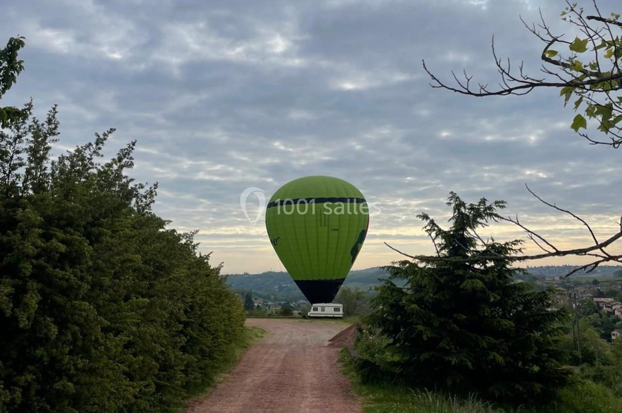 Montgolfière verte posée sur un chemin de terre entouré de végétation sous un ciel nuageux.