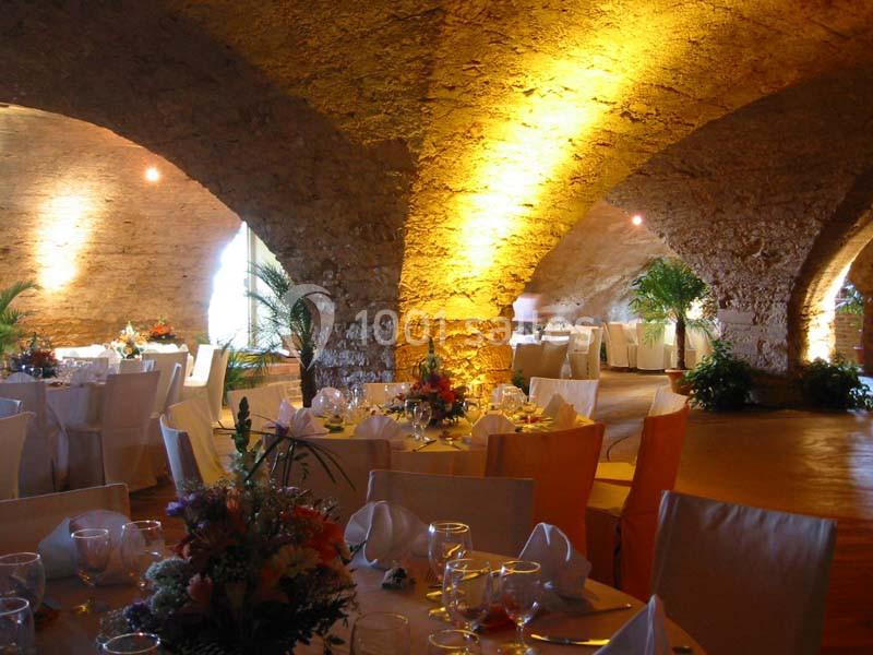 Salle voûtée en pierre éclairée, aménagée avec des tables décorées pour un événement festif.