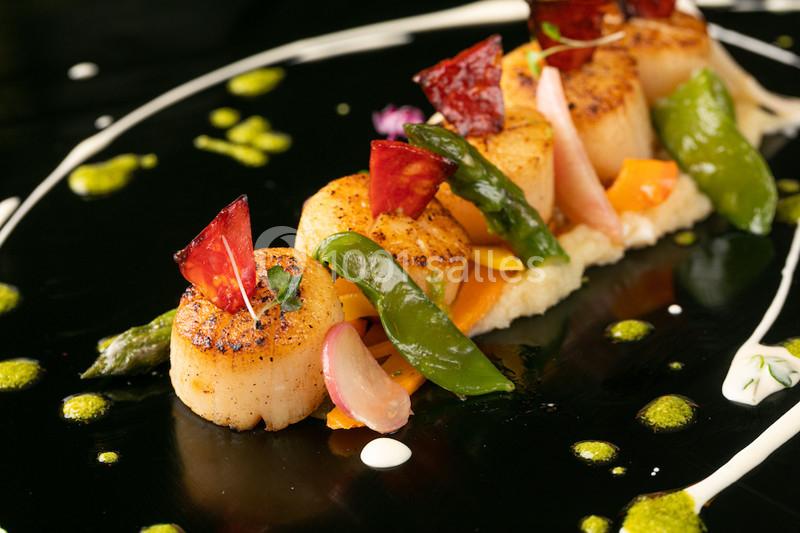 Assiette gastronomique avec des noix de Saint-Jacques grillées, légumes colorés et décorations artistiques.