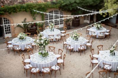 Tables décorées pour un événement en plein air, disposées devant une maison aux volets bleus et murs couverts de lierre.