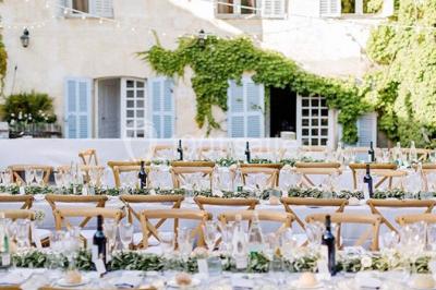 Tables décorées pour un événement en plein air, disposées devant une maison aux volets bleus et murs couverts de lierre.