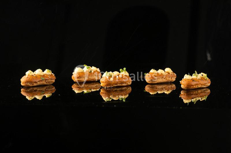 Quatre amuse-bouches disposés en ligne sur une surface noire réfléchissante, garnis de crème et de fines herbes.