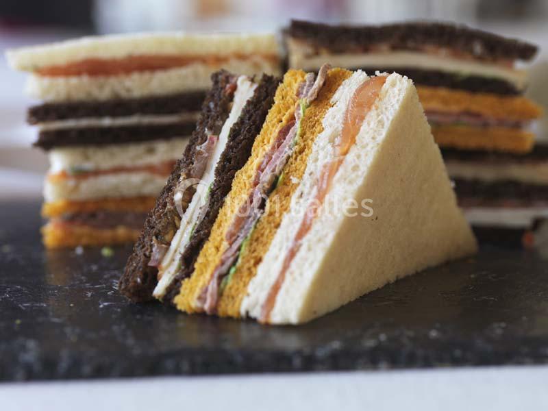 Assortiment de sandwichs triangulaires avec différentes couches de pain et garnitures sur une ardoise noire.