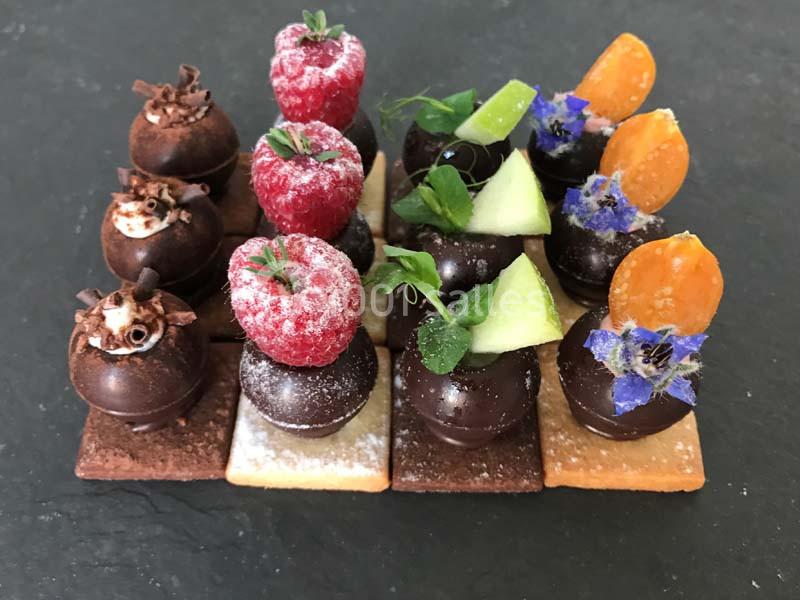 Assortiment de mignardises chocolatées décorées de fruits frais, fleurs comestibles et feuilles sur des biscuits.