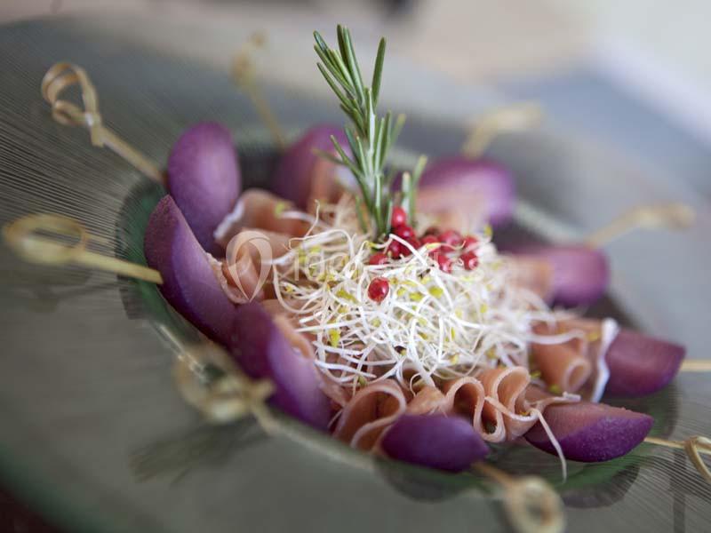 Assiette garnie de tranches de jambon, germes de luzerne, quartiers de figues et brins de romarin, présentée sur des pics.