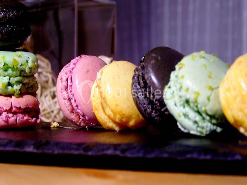 Assortiment de macarons colorés alignés sur une ardoise noire, avec un fond flou et des tons chaleureux.