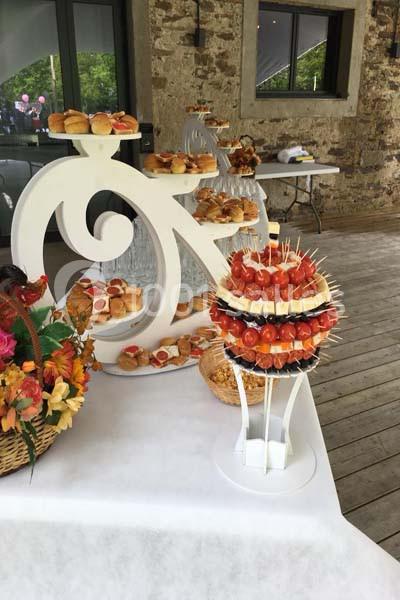 Plateau de buffet avec brochettes apéritives, pains et décorations florales sur une table en bois près d'un mur en pierre.