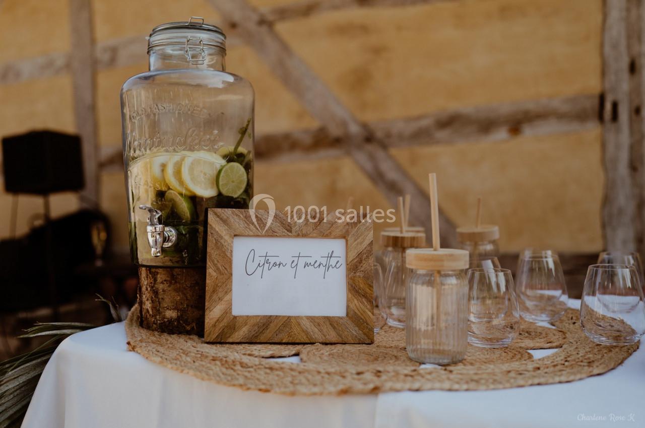 Distributeur de boisson citron-menthe avec verres et pailles en bois sur une table décorée.