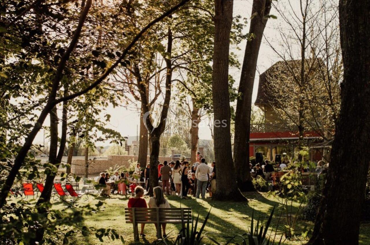 Groupe de personnes réunies dans un jardin ombragé avec des arbres, des chaises longues et une maison en arrière-plan.