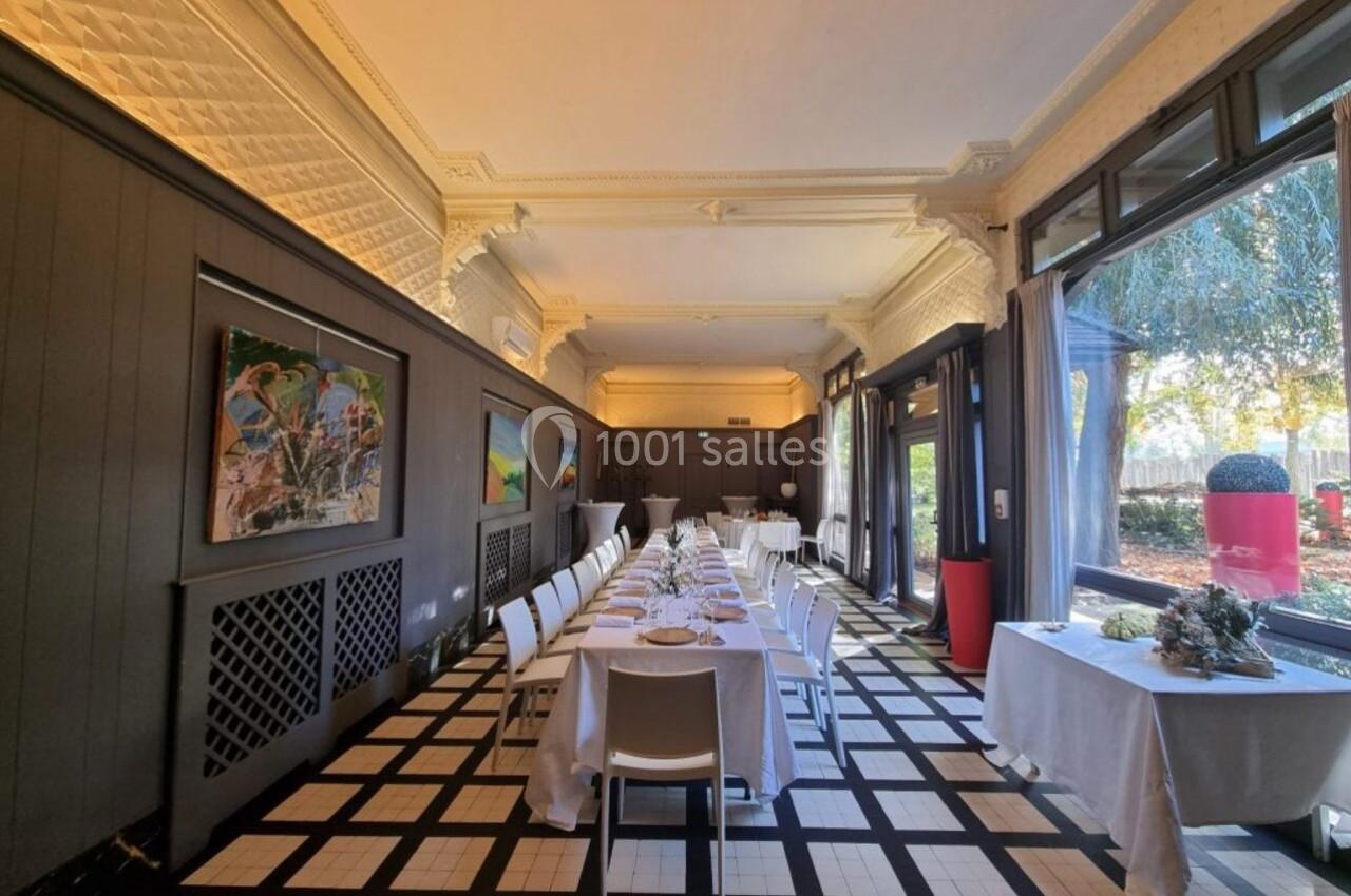 Salle lumineuse avec tables dressées en enfilade, grandes baies vitrées, œuvres d'art accrochées aux murs.