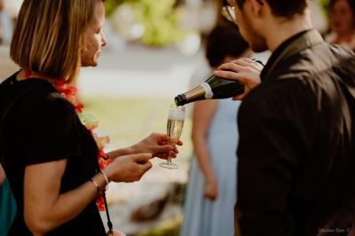 Un chef cuisine sur un brasero dans un jardin, entouré de tables et de végétation.