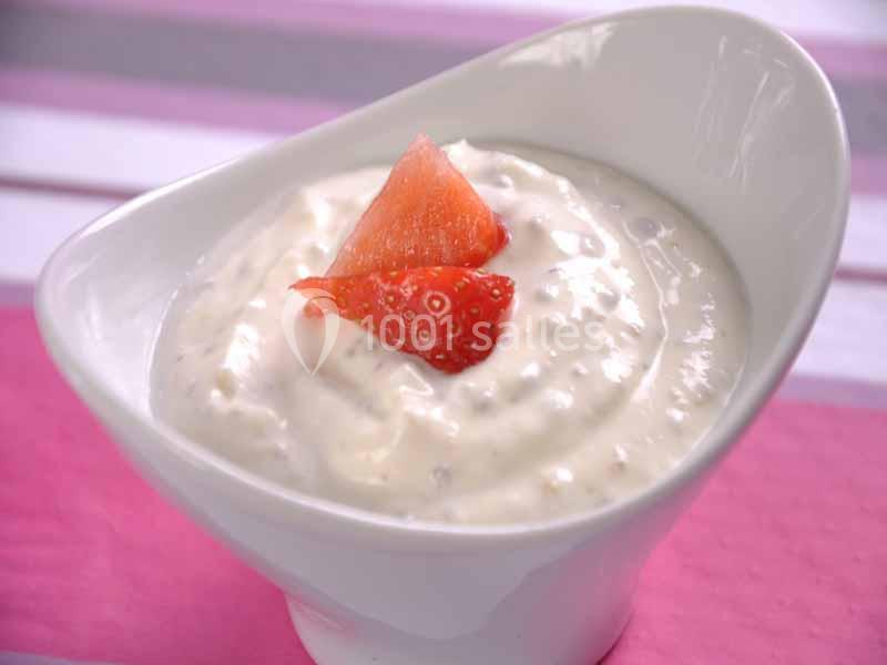 Bol de yaourt crémeux garni de morceaux de fraise, posé sur une surface rose et blanche.