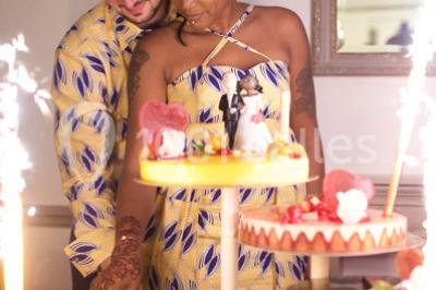 Un couple coupe un gâteau de mariage entouré de desserts décorés et de cierges magiques allumés.