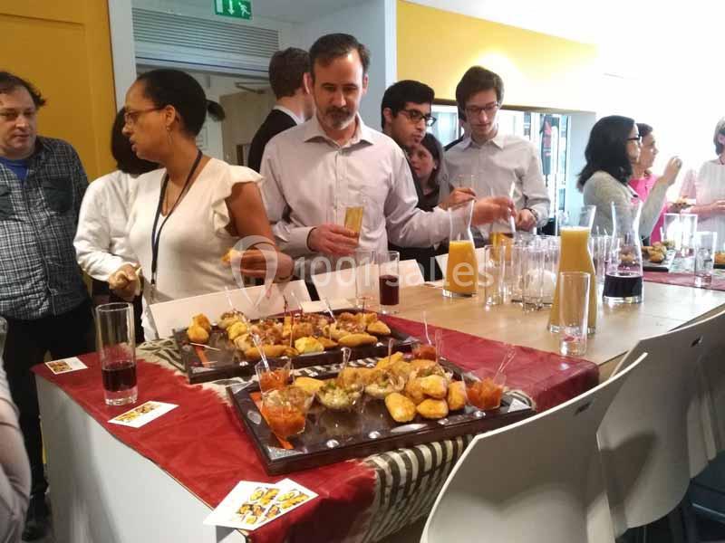 Des personnes se servent à un buffet avec des boissons et des amuse-bouches dans un espace lumineux.