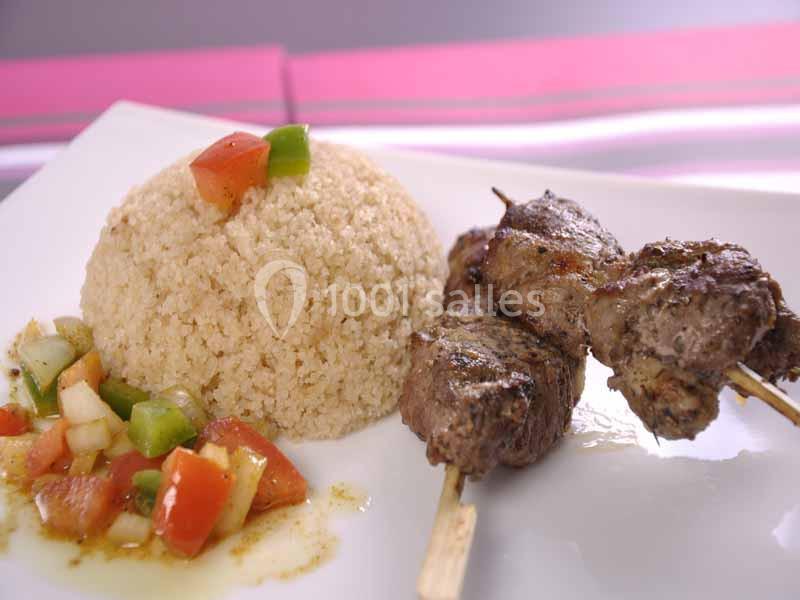 Assiette contenant des brochettes de viande grillée, du couscous et une salade de légumes frais.