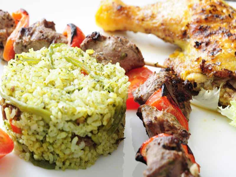 Assiette composée de brochettes de viande, d'un pilaf de riz aux légumes et d'une cuisse de poulet grillée.