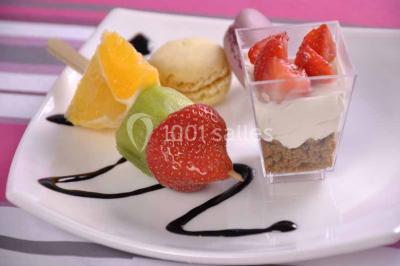 Plateau de verrines colorées garnies de fruits frais comme kiwi, fraise et mangue, tenu par une personne.