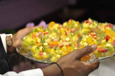 Plateau de verrines colorées garnies de fruits frais comme kiwi, fraise et mangue, tenu par une personne.