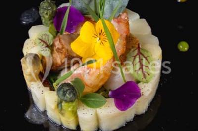 Boule croustillante sur lit de salade, garnie d'une framboise et décorée de sauce rouge sur assiette blanche.