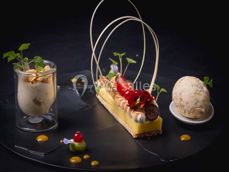 Dessert gastronomique composé d'une tartelette décorée, d'une glace et d'une mousse présentés sur une assiette noire.