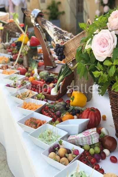 Buffet coloré avec légumes, fruits, fleurs et paniers en osier disposés sur une table blanche en extérieur.