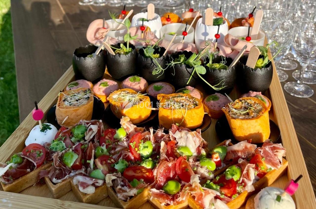 Plateau de bouchées apéritives variées avec charcuterie, légumes, verrines et décorations colorées.