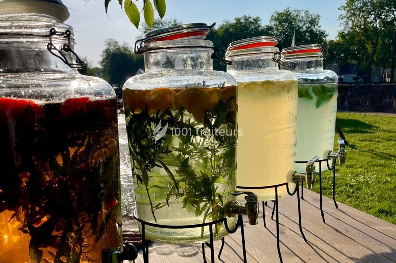 Bocaux en verre remplis de boissons infusées aux fruits et herbes, disposés sur une table en extérieur.