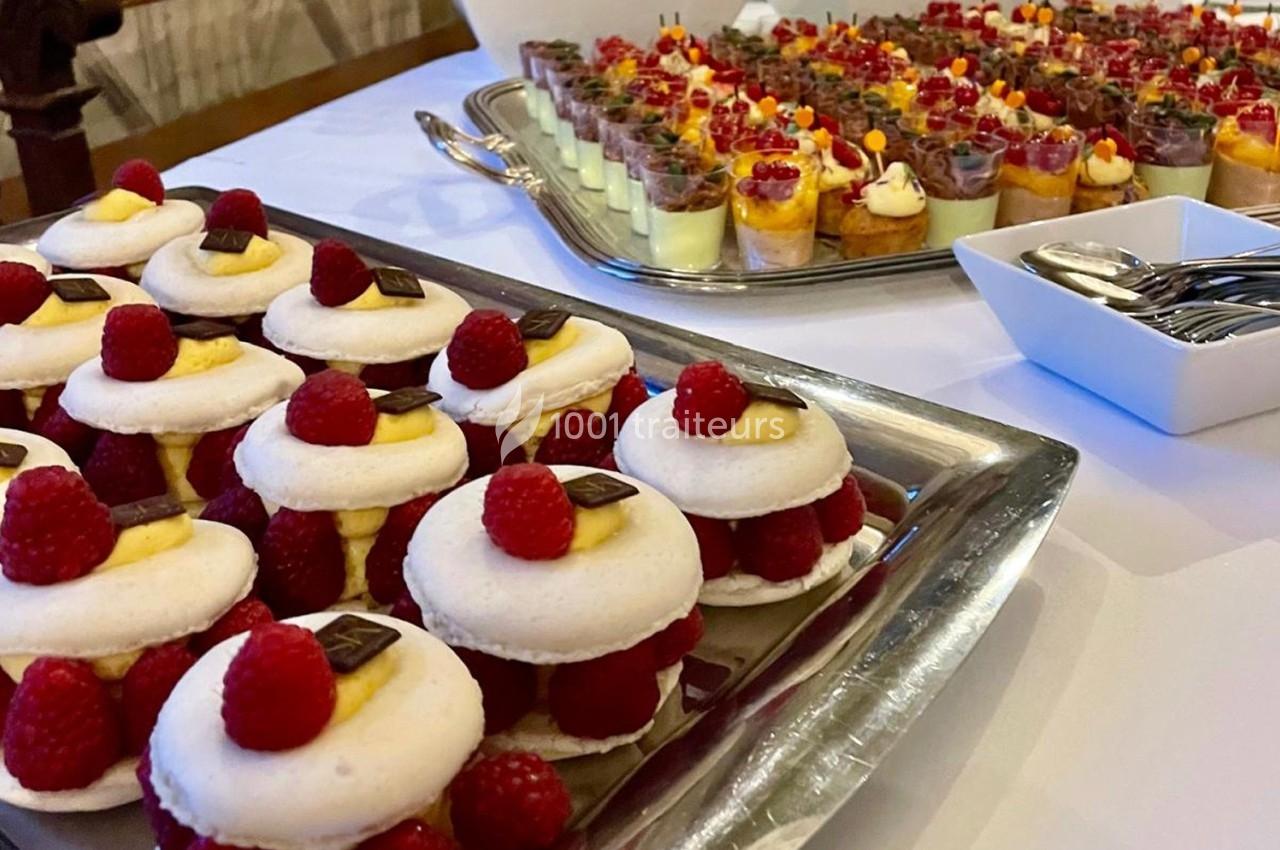 Plateaux de desserts variés avec macarons garnis de framboises et verrines colorées sur une table dressée.