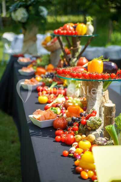 Table garnie de légumes et fruits colorés disposés sur des présentoirs en extérieur.