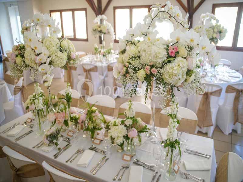 Salle de réception décorée avec des compositions florales blanches et roses sur des tables élégamment dressées.