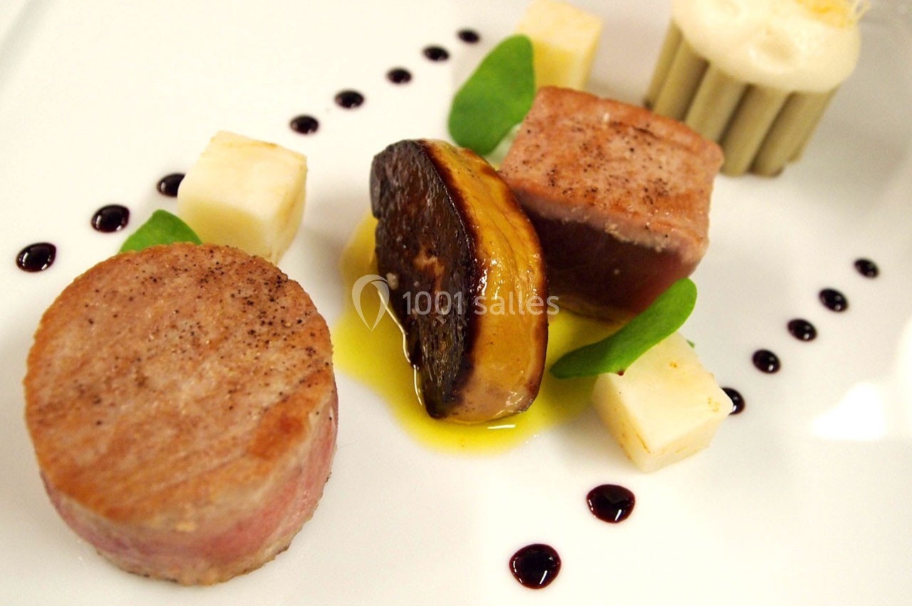 Assiette gastronomique composée de viande, foie gras, cubes de fromage, sauce et décorations de gouttes de réduction.