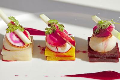 Assiette gastronomique avec trois noix de Saint-Jacques sur des légumes colorés, décorée de fines tranches et d'herbes.