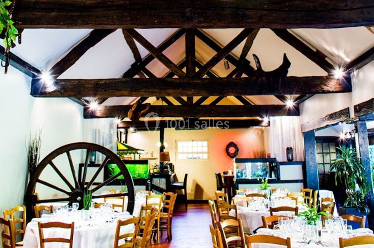 Salle de restaurant avec poutres apparentes, tables dressées et décoration rustique comprenant une roue en bois.