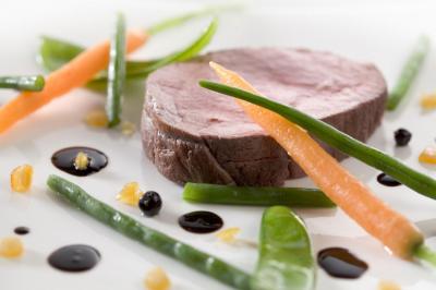 Tranche de viande cuite accompagnée de haricots verts, carottes et gouttes de sauce sur une assiette blanche.