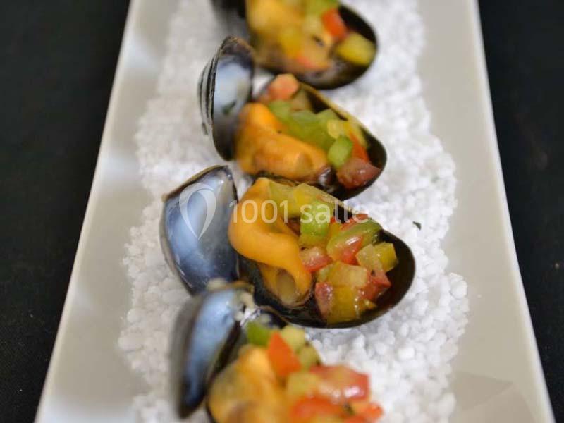 Moules ouvertes garnies de légumes colorés, présentées sur un lit de sel blanc dans une assiette rectangulaire.