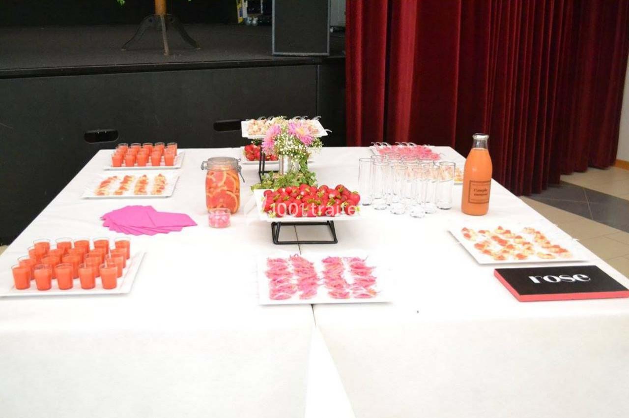 Table dressée avec des verrines, fraises, boissons et décorations roses, dans un cadre intérieur.