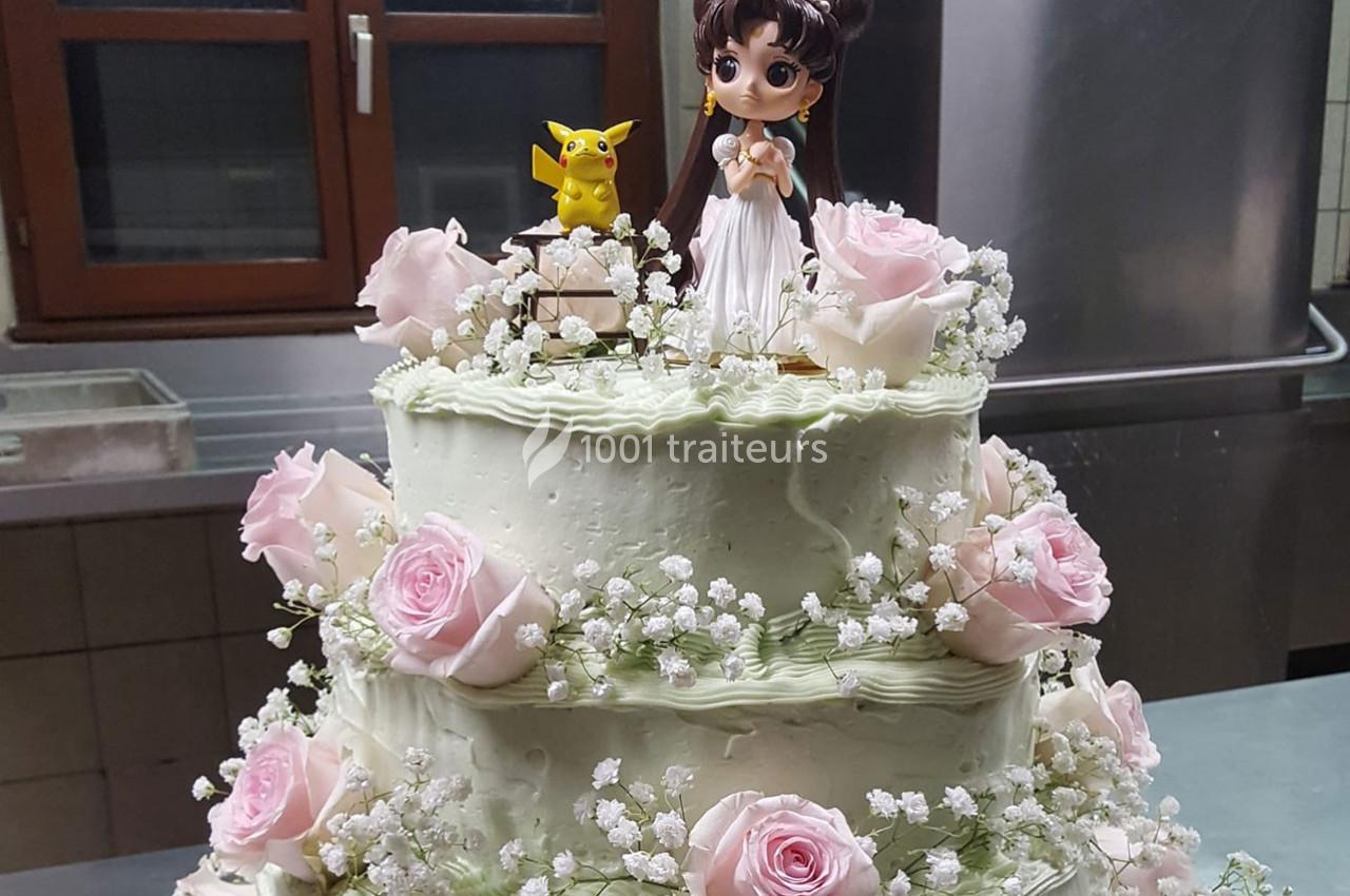 Gâteau à étages décoré de roses roses, gypsophiles et figurines, dont un personnage animé et un Pikachu.
