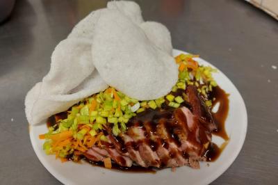 Assiette de magret de canard tranché, nappé de sauce, garni de légumes émincés et accompagné de chips de crevettes.