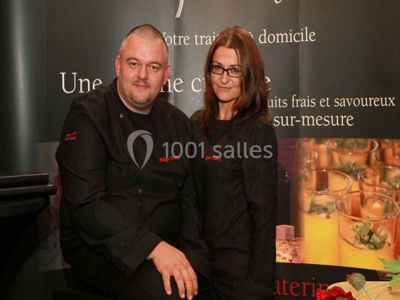 Un homme et une femme en tenue de chef posent devant un panneau promotionnel de service traiteur.